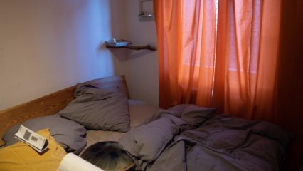 Leeres, unordentliches Bett und orangene Gardinen