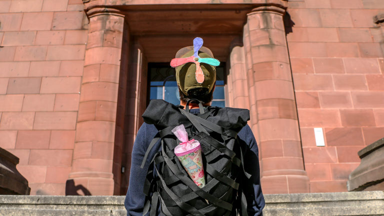 Student mit Schultüte und Propeller-Kappe vor Unigebäude